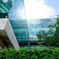 Bâtiment moderne en verre et en béton, entouré de verdure avec un ciel bleu partiellement nuageux en arrière-plan.